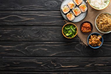 top view of bowls with tasty korean side dishes near gimbap on wooden surface  clipart