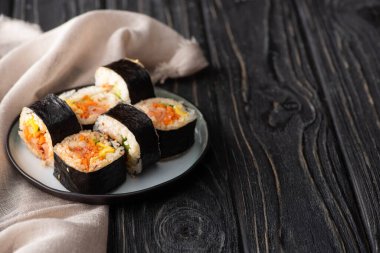selective focus of tasty rice rolls with vegetables and salmon near cotton napkin on wooden surface  clipart