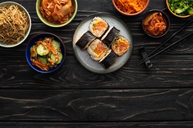 Tahta yüzeyde, lezzetli Kore mezelerinin yanında japon ve yemek çubuklarıyla tabağın üst görüntüsü. 
