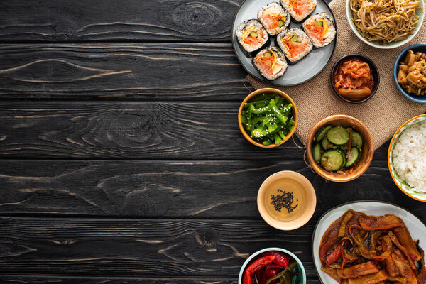 top view of tasty korean side dishes near gimbap and sesame oil on wooden surface 