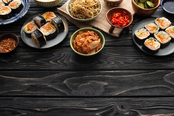 plates with fresh gimbap near korean side dishes on wooden surface 
