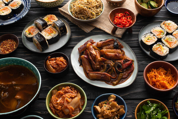 plates and bowls with korean side dishes and gimbap  on wooden surface 