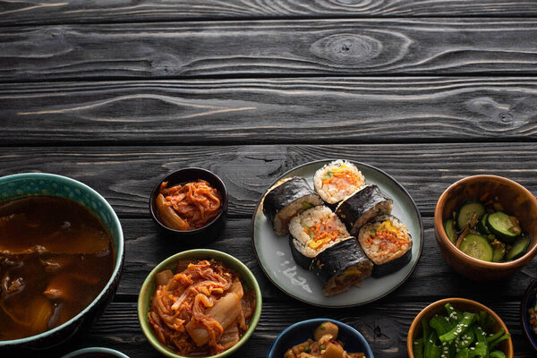 top view of plate with fresh gimbap near korean side dishes and soup on wooden surface 