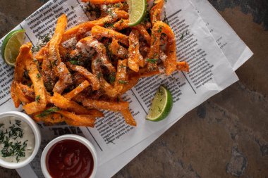 top view of tasty french fries and sliced lime on newspaper and marble surface   clipart