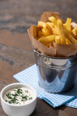 Lezzetli patates kızartması ve mermer yüzeyde kremalı sarımsak sosu olan bir kova. 