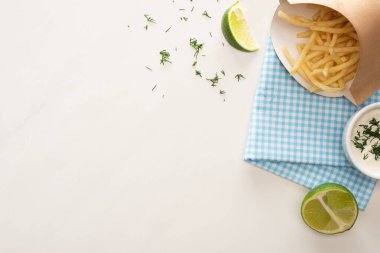 Sarımsak sosunun yanında gevrek patates kızartması ve dilimlenmiş limonla kutunun üst görüntüsü. 