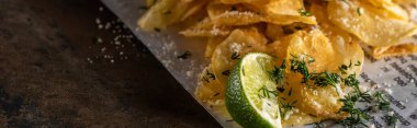 panoramic shot of crunchy potato chips with salt near sliced lime and newspaper on marble surface  clipart