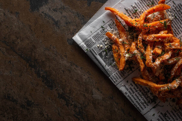 вид соленой картошки фри на газету с текстом на мраморной поверхности
  