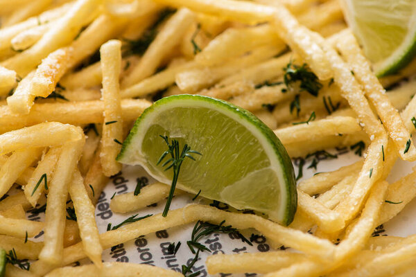 close up of lime near crispy french fries with dill 