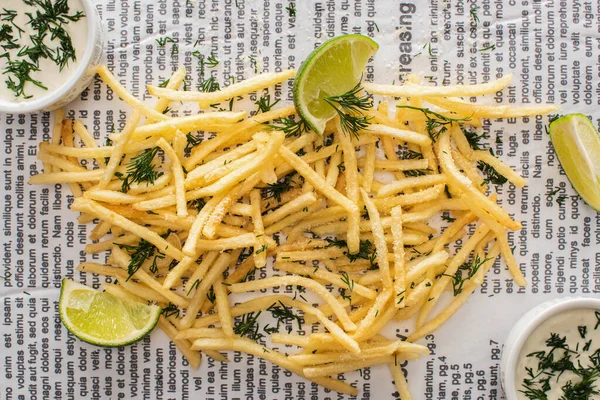 Top view of crispy french fries with dill near lime and garlic sauce on newspaper — Stock Image Top View Crispy French Fries Dill Lime Garlic Sauce Newspaper Stock Photo