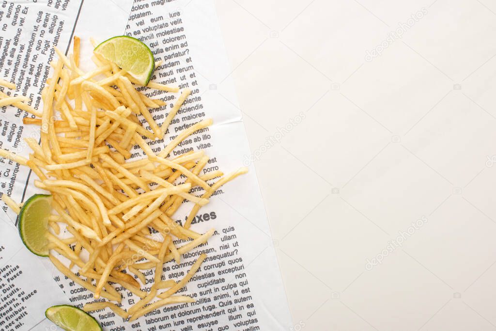 top view of crispy french fries and sliced lime on newspaper on white 