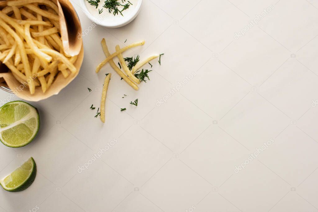 top view of crispy french fries, garlic sauce and sliced lime on white 