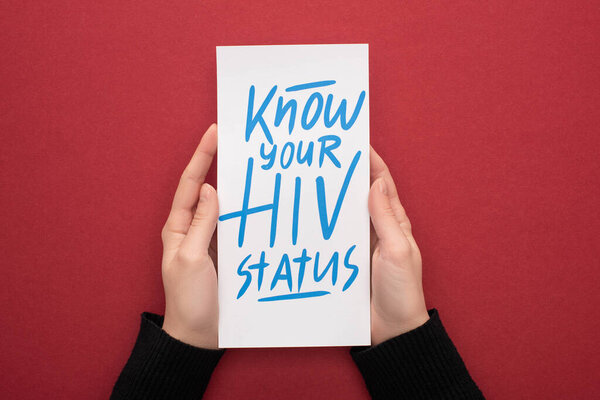 cropped view of woman holding card with know your HIV status lettering on red background