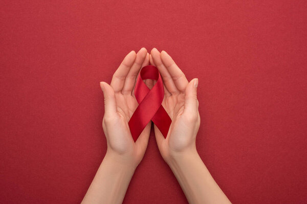 cropped view of woman holding red awareness aids ribbon on red background