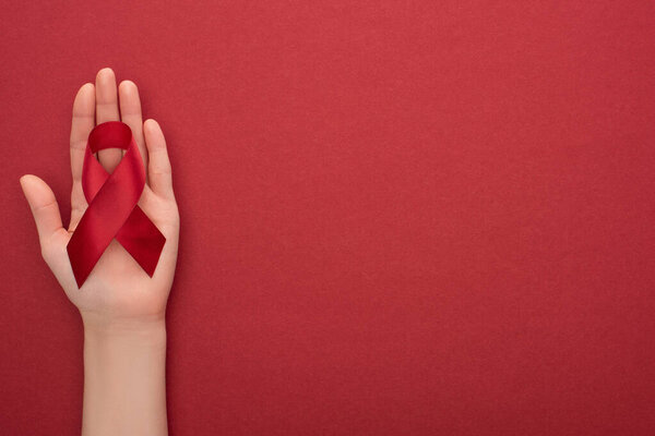 cropped view of woman holding red awareness aids ribbon on red background