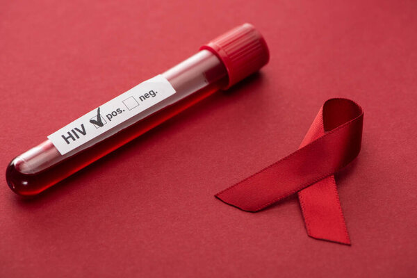 red awareness aids ribbon and positive hiv blood sample test on red background