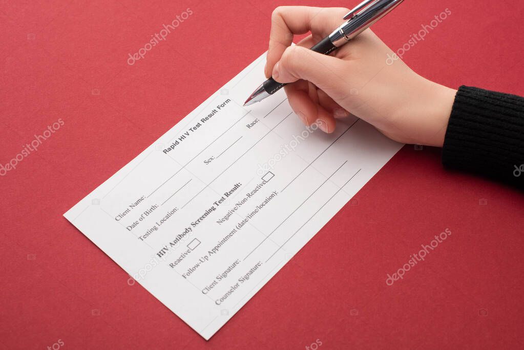 partial view of woman filling in rapid HIV test result form on red background