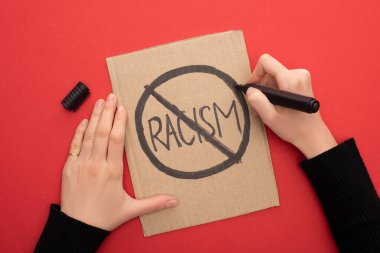 cropped view of woman writing stop racism sign with marker on carton placard on red background clipart