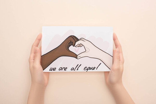 cropped view of woman holding picture with drawn multiethnic hands showing heart gesture on beige background