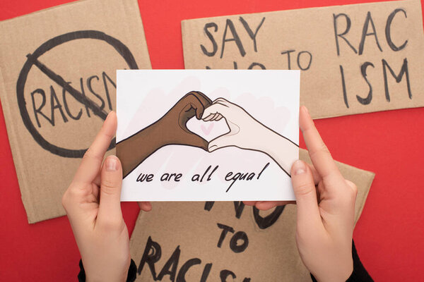 cropped view of woman holding picture with drawn multiethnic hands showing heart gesture on red background with placards