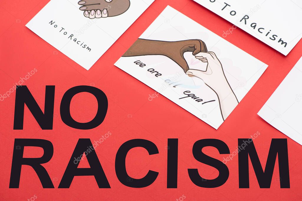 top view of black no racism lettering among pictures with multiethnic hands on red background