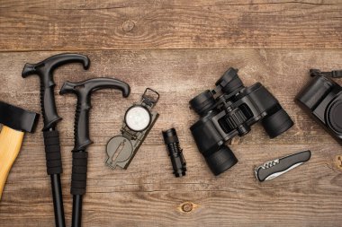 top view of axe, trekking poles, compass, flashlight, binoculars, jackknife and photo camera on wooden table  clipart