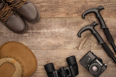 Çizmelerin, şapkanın, dürbünün, fotoğraf makinesinin ve tahta yüzeydeki yürüyüş direklerinin üst görüntüsü