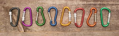 panoramic shot of colorful carabiners on wooden table clipart