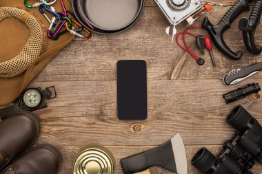 Tahta masadaki yürüyüş ekipmanlarının yanında siyah ekranlı akıllı telefonun üst görüntüsü