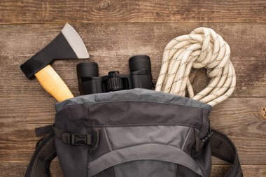 top view of backpack with axe, hiking rope and binoculars on wooden surface clipart