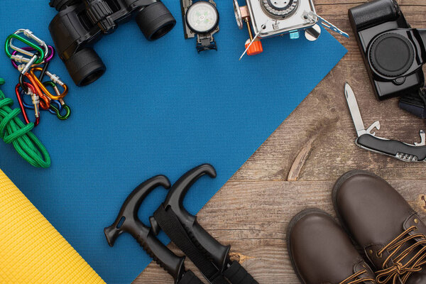 top view of hiking equipment on blue sleeping mat, photo camera and boots on wooden table