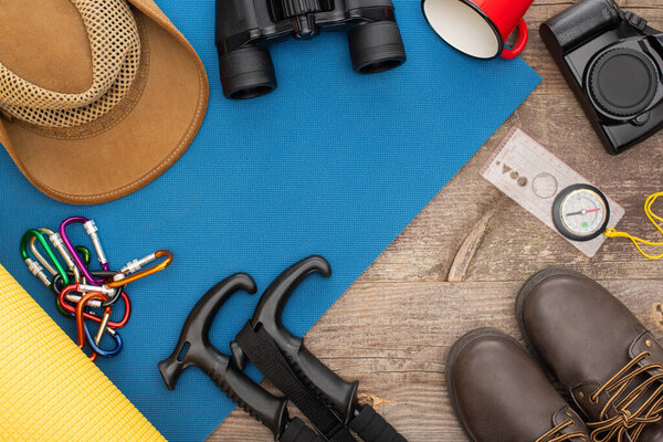 top view of hiking equipment on blue sleeping pad, photo camera, boots and hat on wooden surface