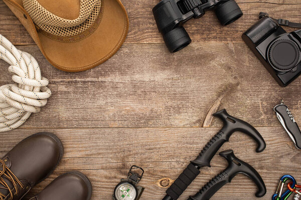 верхний вид туристического оборудования, сапоги, шляпы и фотокамеры на деревянной поверхности
