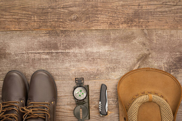 top view of boots, compass, jackknife and hat on wooden table