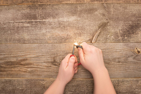 частичный вид человека, освещающего искру на деревянном столе
