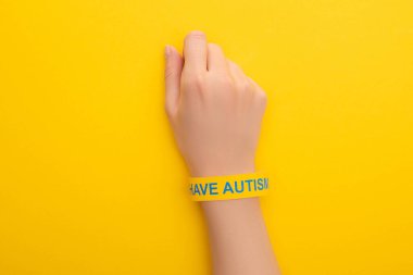 top view of woman hand in bracelet with I have autism inscription on yellow clipart