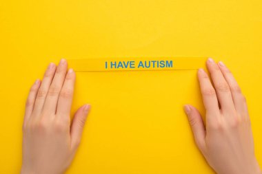 partial view of woman holding bracelet with I have autism inscription on yellow clipart