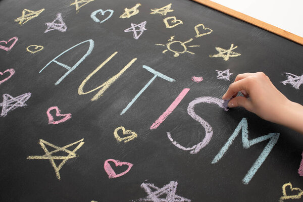 частичный взгляд женщины, пишущей слово аутизм на доске с сердцами, звездами и солнцами
