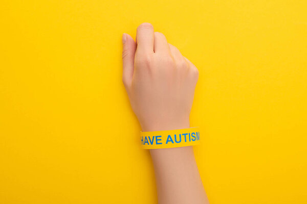 top view of woman hand in bracelet with I have autism inscription on yellow