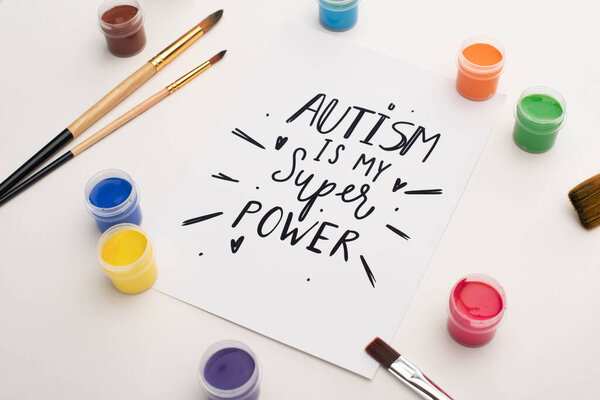 paints, brushes and card with autism is my super power lettering on white 