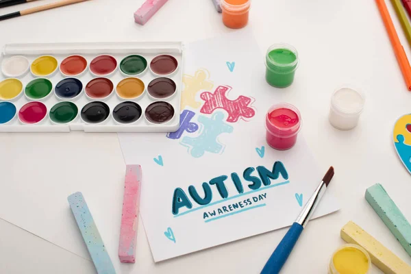 card with Autism Awareness Day lettering and painting of puzzle on white with paints and chalks