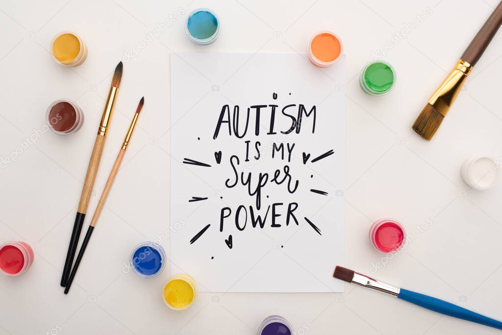 top view of paints, brushes and card with autism is my super power lettering on white