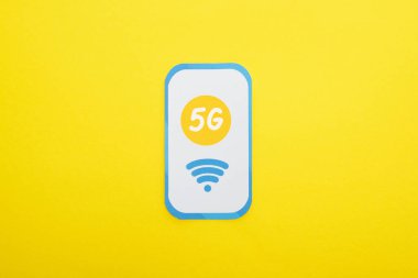 Sarı arkaplandaki kağıt akıllı telefondaki 5G harflerinin üst görünümü