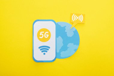 Sarı arka planda, dünyanın yakınındaki kağıt akıllı telefondaki 5G harflerinin üst görünümü