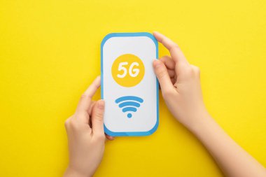 Sarı arka planda 5G harfli kağıt akıllı telefon tutan kadın görüntüsü.