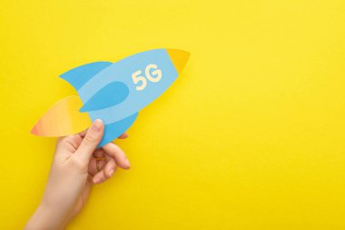 Kırpılmış, sarı arka planda 5 G harfli kağıt roket tutan kadın görüntüsü.