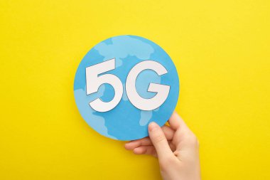 Sarı arka planda 5 G harfli küreyi tutan kadının kırpılmış görüntüsü