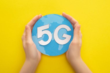 Sarı arka planda 5 G harfli küreyi tutan kadının kırpılmış görüntüsü