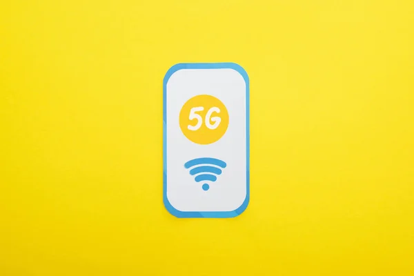 黄色の背景の紙のスマートフォンの5Gレタリングのトップ表示 — ストック写真
