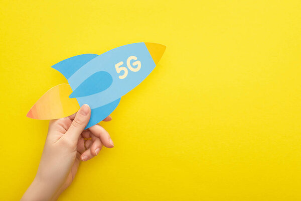 cropped view of woman holding paper rocket with 5g lettering on yellow background